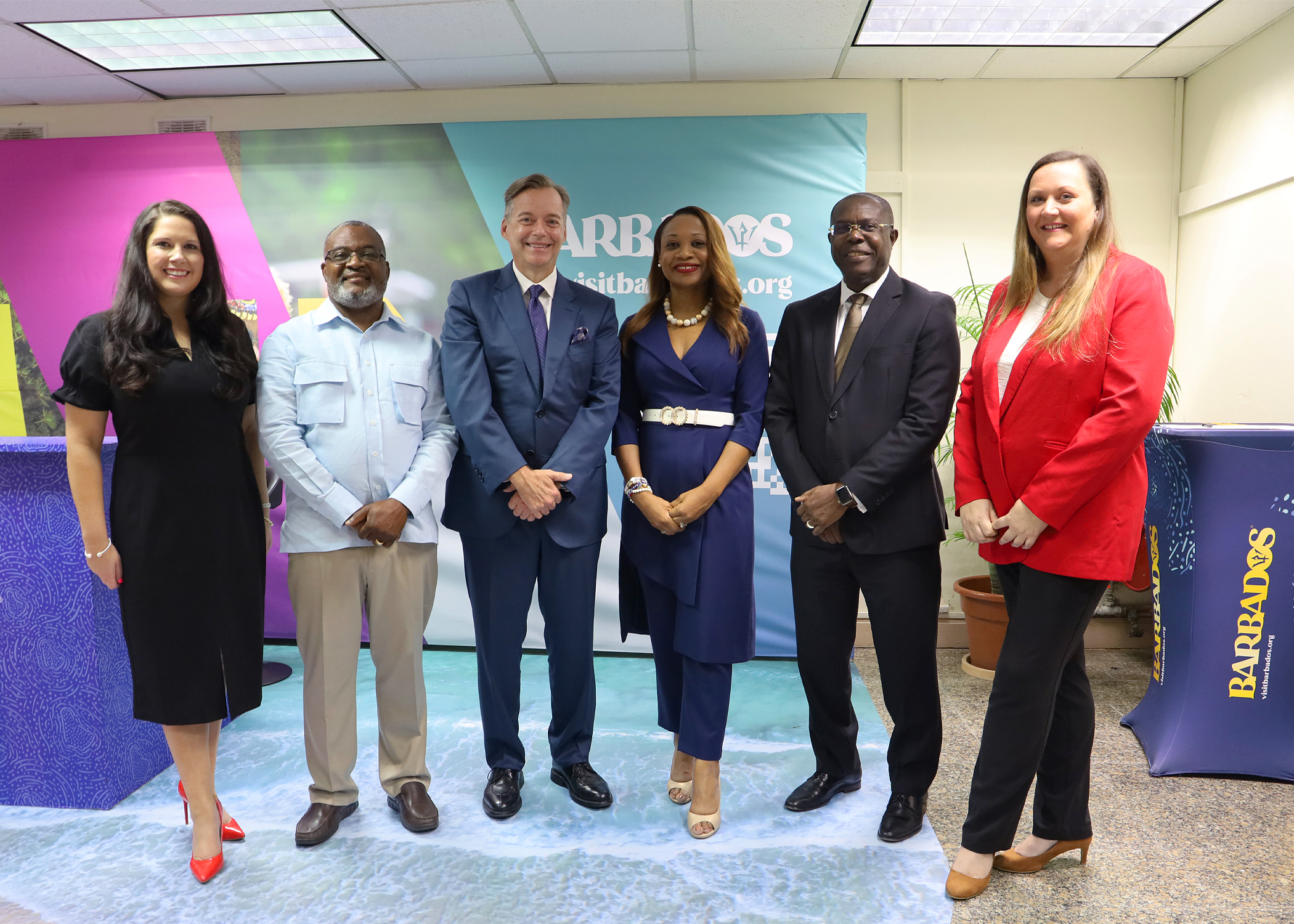 Group of six persons including CDB Acting President standing in a row in front of Barbados signage