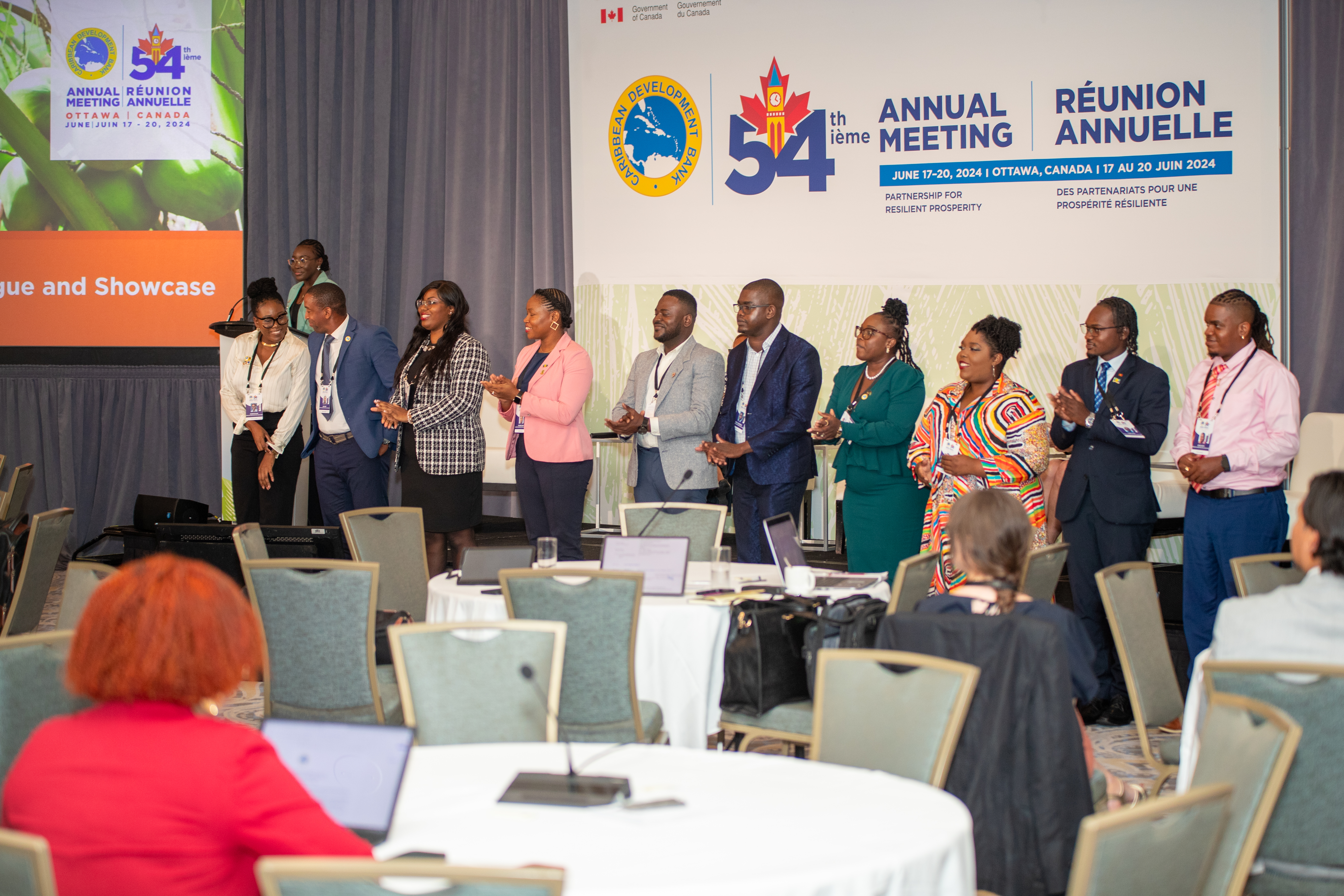 A group of young people standing on a stage against the CDB 54th Annual Meeting backdrop