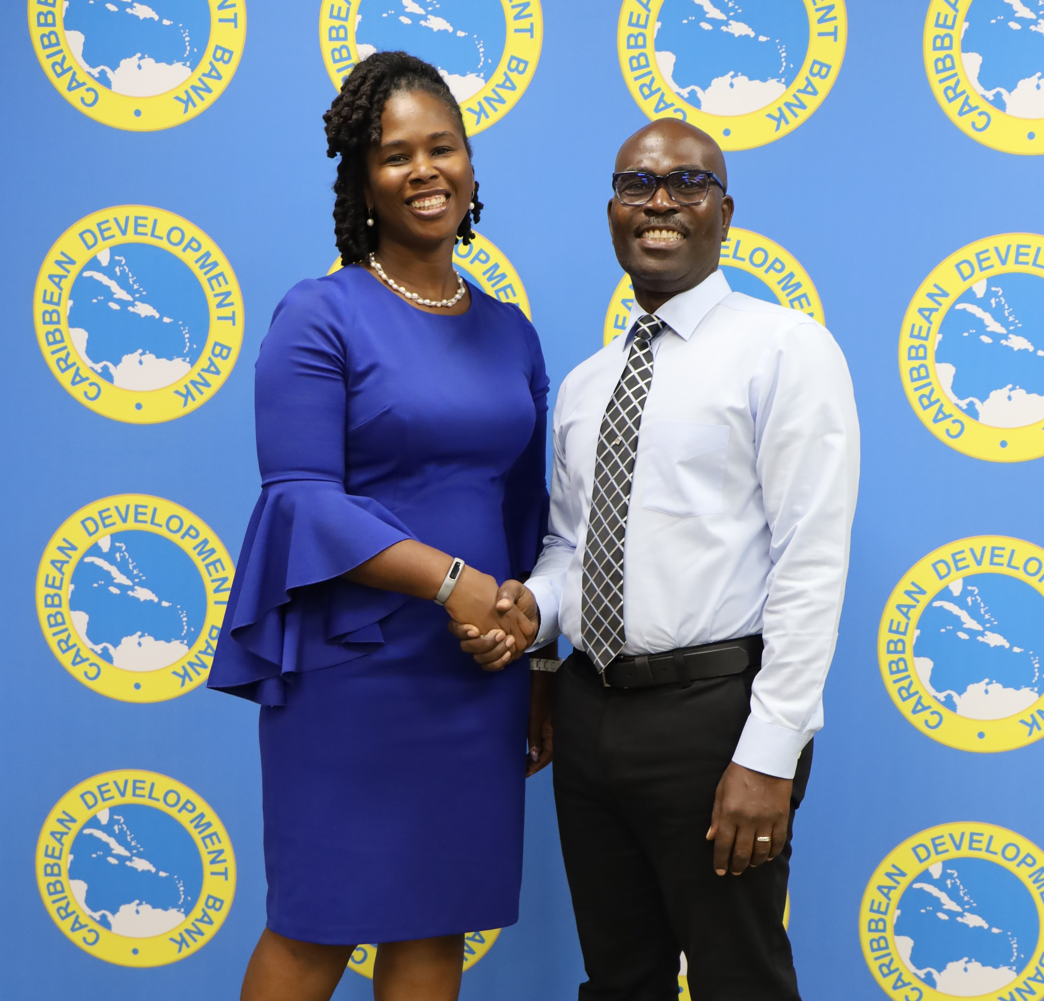 Lady in blue dress and man in white shirt black pants and tie standing shaking hands