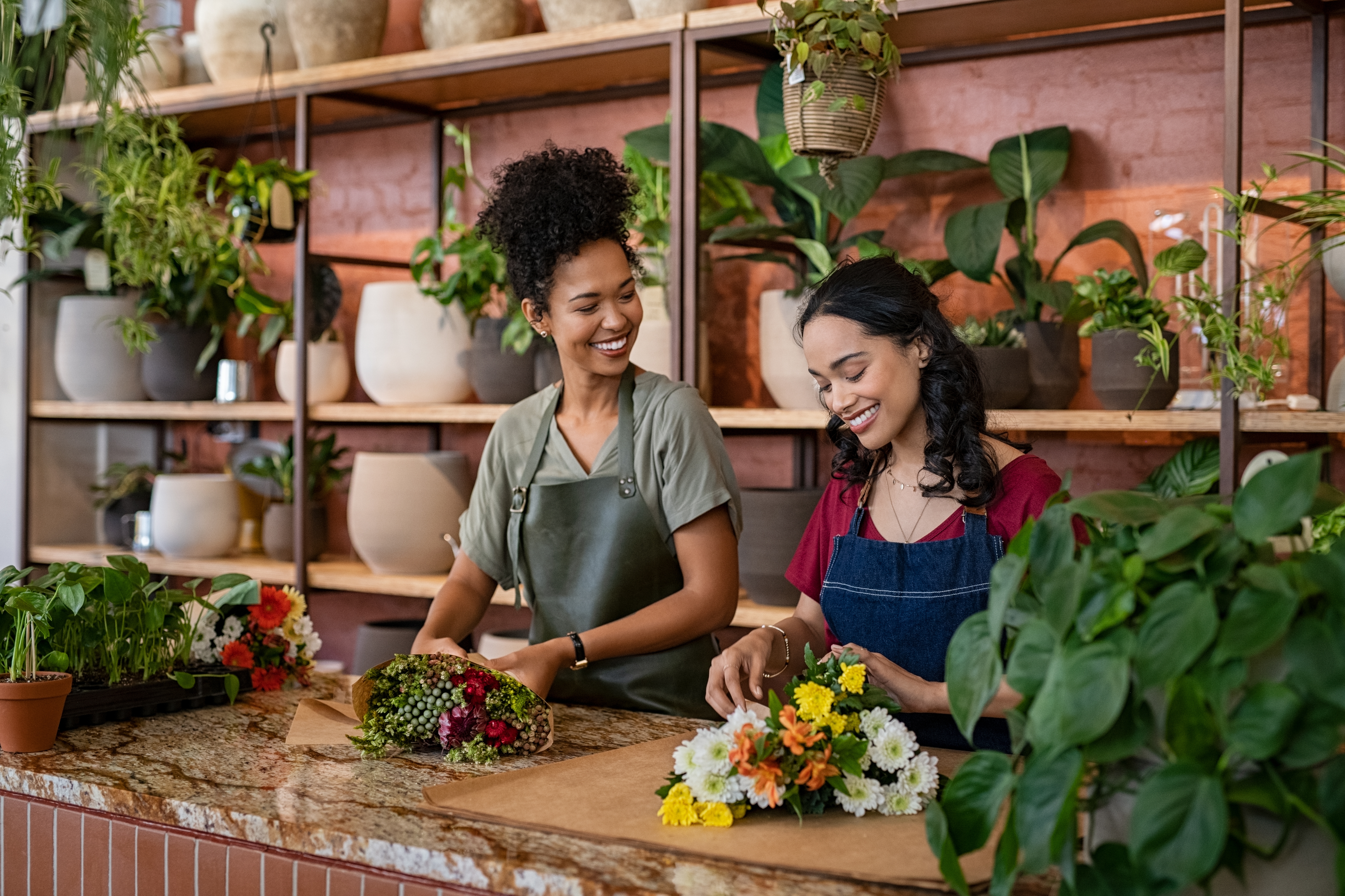 Two happy and smiling young woman florist working together in flower shop. 