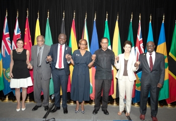 A group of people standing on a platform holding hands with various flags flying behind them