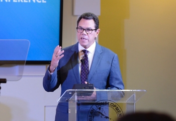 Dr. Smith in a blue suit standing at the lectern delivering his remarks at the Annual News Conference